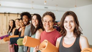 class of yoga students smiling and holding mats in hand