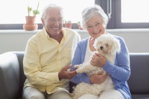 elderly couple holding there small white dog while smiling