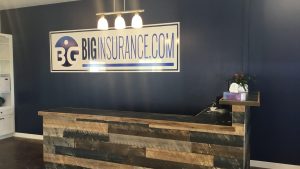 BIG Insurance Receptionist Area with logo and dark blue background. Desk is made of reclaimed wood