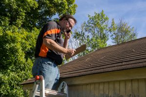 Contractor On Ladder Figuring Hail Damage Repair cost To Roof