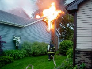 Fire fighter putting water on home fire with large hose